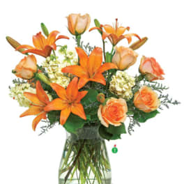 Orange lilies and peach roses with cream flowers arranged in a clear glass vase
