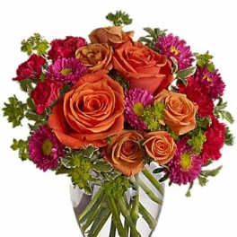 Orange roses and magenta daisies in a clear glass vase