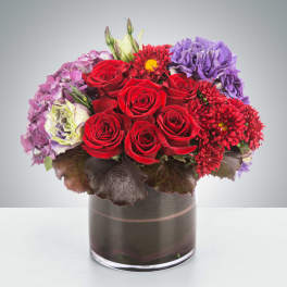 Red roses with purple and pink flowers in a glass vase