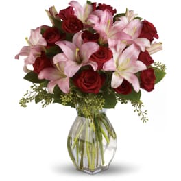 Arrangement of pink lilies and red roses in a clear glass vase with water