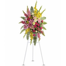 Standing spray of pink lilies, yellow blooms, roses and carnations on a white easel