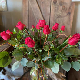 Tall arrangement of red roses with foliage in a clear glass vase on a rustic wooden background