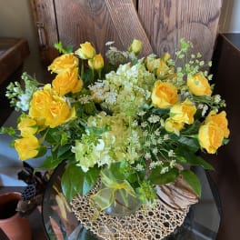 Medium arrangement of yellow roses and pale green hydrangeas in a clear glass vase