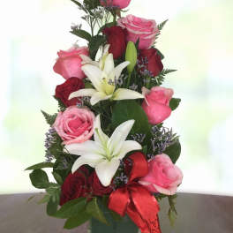 Pink and red roses with white lilies in a glass vase