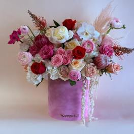 Mixed bouquet of roses, orchids, and ranunculus in a pink hat box