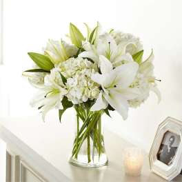 White lilies and hydrangeas arranged in a clear glass vase.