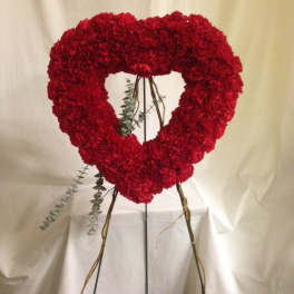 Heart-shaped red floral wreath on a stand with trailing greenery