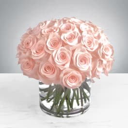 A round bouquet of pale pink roses in a clear glass vase.