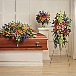 Colorful floral funeral casket spray with standing wreaths and arrangements