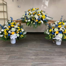 Three floral funeral arrangements with white, yellow, and blue flowers