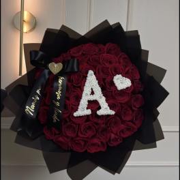 Round bouquet of deep red roses with black wrapping and a white letter A