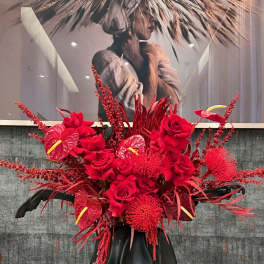 Large red floral arrangement in a black vase with roses and anthuriums