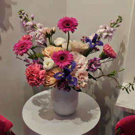 Mixed bouquet of pink, peach, white, and purple flowers in a white vase