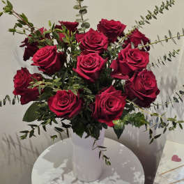 Bouquet of deep red roses in a white vase with airy greenery