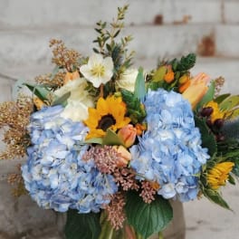 Mixed bouquet with blue hydrangeas, sunflowers, and tulips in a glass vase