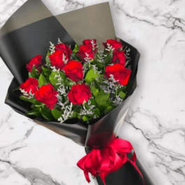 Bouquet of red roses with white filler flowers wrapped in black paper and tied with a red ribbon