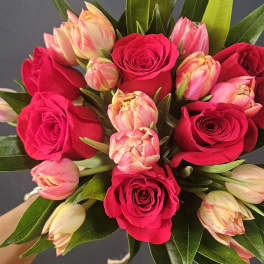 Hand-tied bouquet of hot pink roses and cream-pink tulips against a dark background
