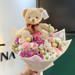 Teddy bear sitting in a pink bouquet of roses and daisies