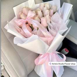 Bouquet of pale pink roses wrapped in white and pink paper with a ribbon