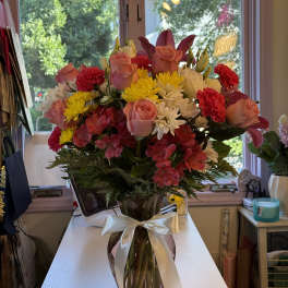 Mixed bouquet of pink roses, yellow and white daisies, and red carnations in a glass vase