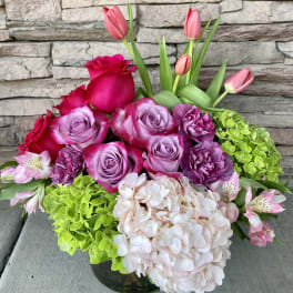 Pink roses, tulips, hydrangeas, and carnations in a low vase