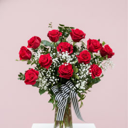 Red roses arranged in a clear glass vase with a striped ribbon