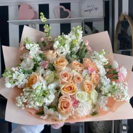 Bouquet of peach and white roses with white filler flowers in pink wrapping