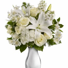 Arrangement of white lilies, roses, carnations, and alstroemeria in a shiny silver vase.