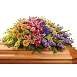 Colorful casket spray with pink lilies, roses, and mixed flowers on a wooden casket