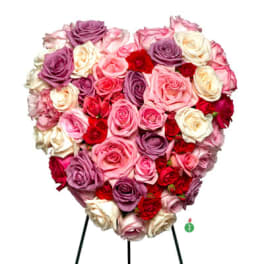 Heart-shaped arrangement of pink, red, lavender, and cream roses on a metal easel stand