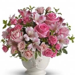 Pink roses and lilies arranged in a white urn vase