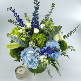 Blue and white floral arrangement in a green vase with a candle beside it