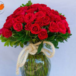 Red roses arranged in a clear glass vase with a rope bow