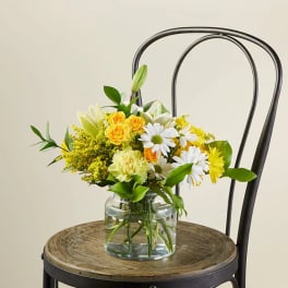 Yellow and white mixed flower arrangement in a clear glass vase on a rustic wooden chair