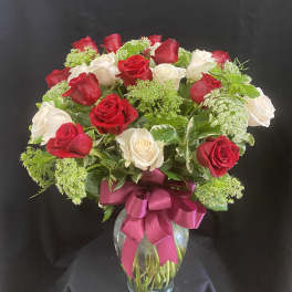 Red and white roses in a glass vase with a pink ribbon