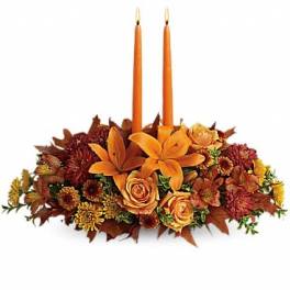 Low fall centerpiece of orange lilies, roses, and mums with two tall orange taper candles