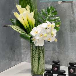 Tall arrangement of white orchids and pale yellow calla lilies in a glass vase