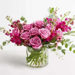 Pink roses and magenta flowers arranged in a clear glass vase