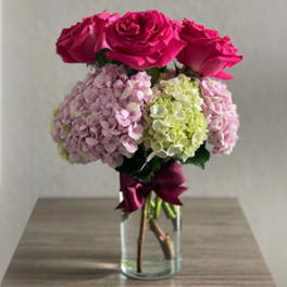 Pink roses and hydrangeas in a clear glass vase with a ribbon