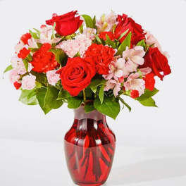 Red roses and pink flowers in a red glass vase