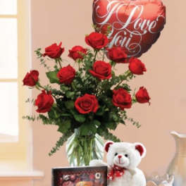 Red roses in a vase with a heart balloon, teddy bear, and chocolates