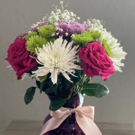 Pink roses and white chrysanthemums in a purple vase with a ribbon