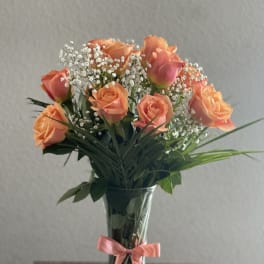 Peach roses in a clear glass vase with a pink ribbon