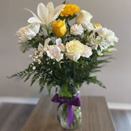 Bouquet of white and yellow flowers in a glass vase with a purple ribbon