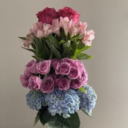 Tall bouquet of pink roses, alstroemeria, and blue hydrangeas in a glass vase