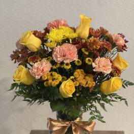 Yellow roses and pink carnations in a glass vase with a gold ribbon