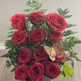 Red roses arranged in a clear square vase with fern accents