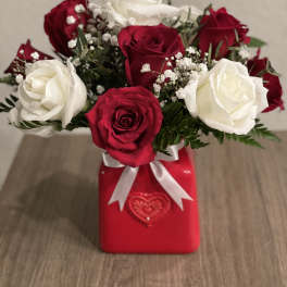 Red and white roses arranged in a red gift box with a white ribbon