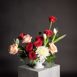 Red and peach roses arranged with white blooms in a white vase