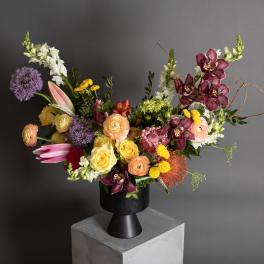 Mixed bouquet in a black vase with roses, orchids, lilies, and purple allium
